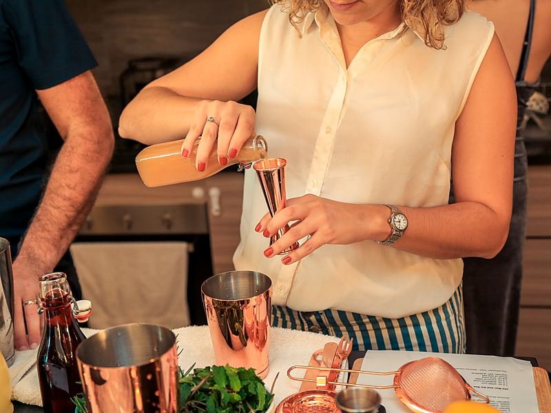 A group learning to make cocktails together at a home kitchen counter with copper barware